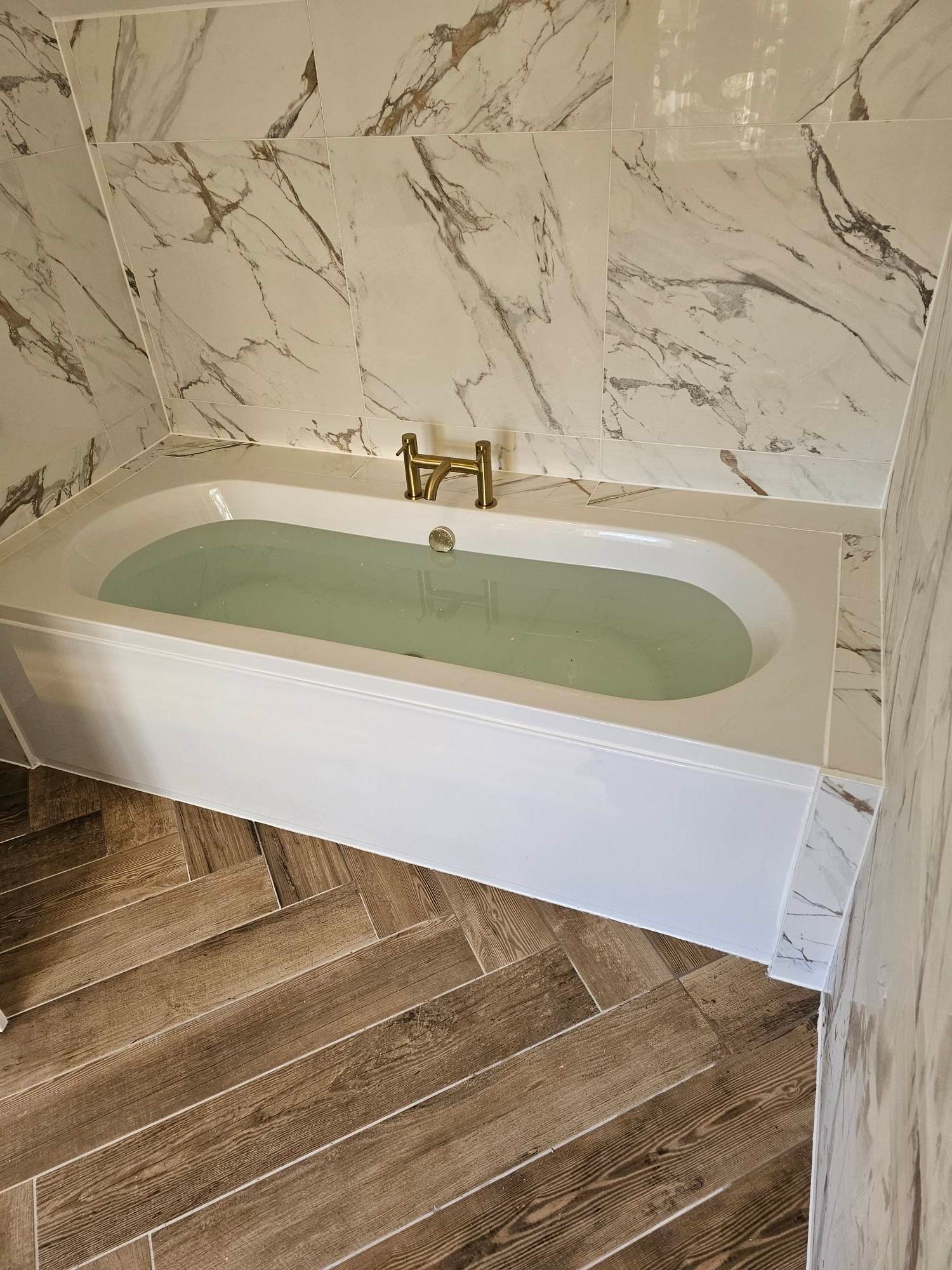 Fitted bath with brass tap and marble-effect wall tiling in Tamworth