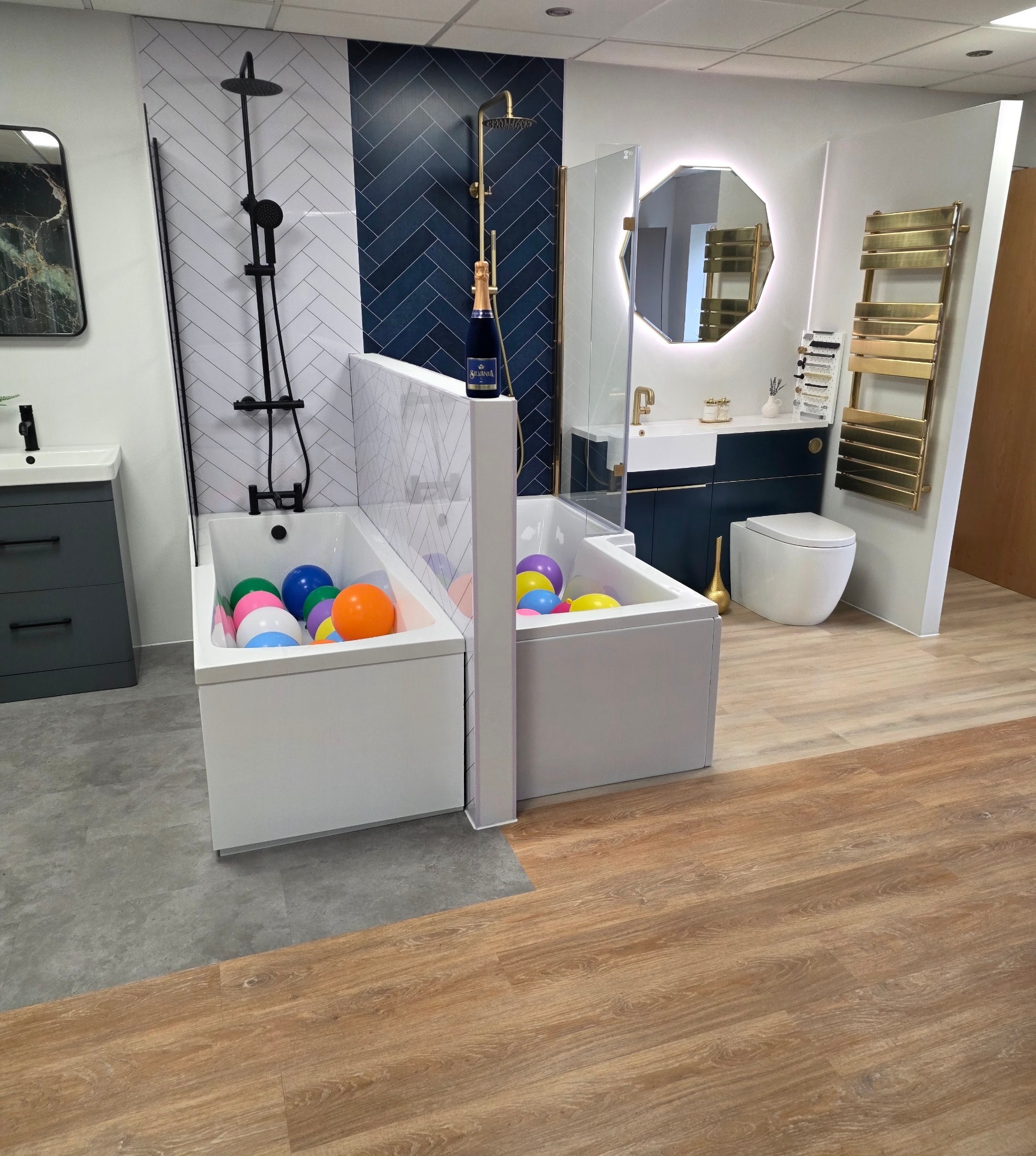 Showroom display in Tamworth featuring a bath, navy herringbone feature wall, brushed gold brassware and backlit octagonal mirror