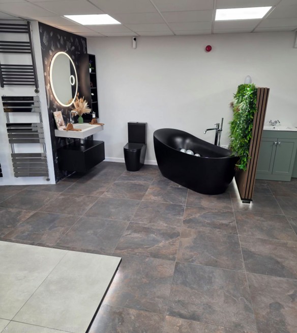 Matt-black freestanding bath with backlit round mirror and chrome towel rail in the Tamworth bathroom showroom